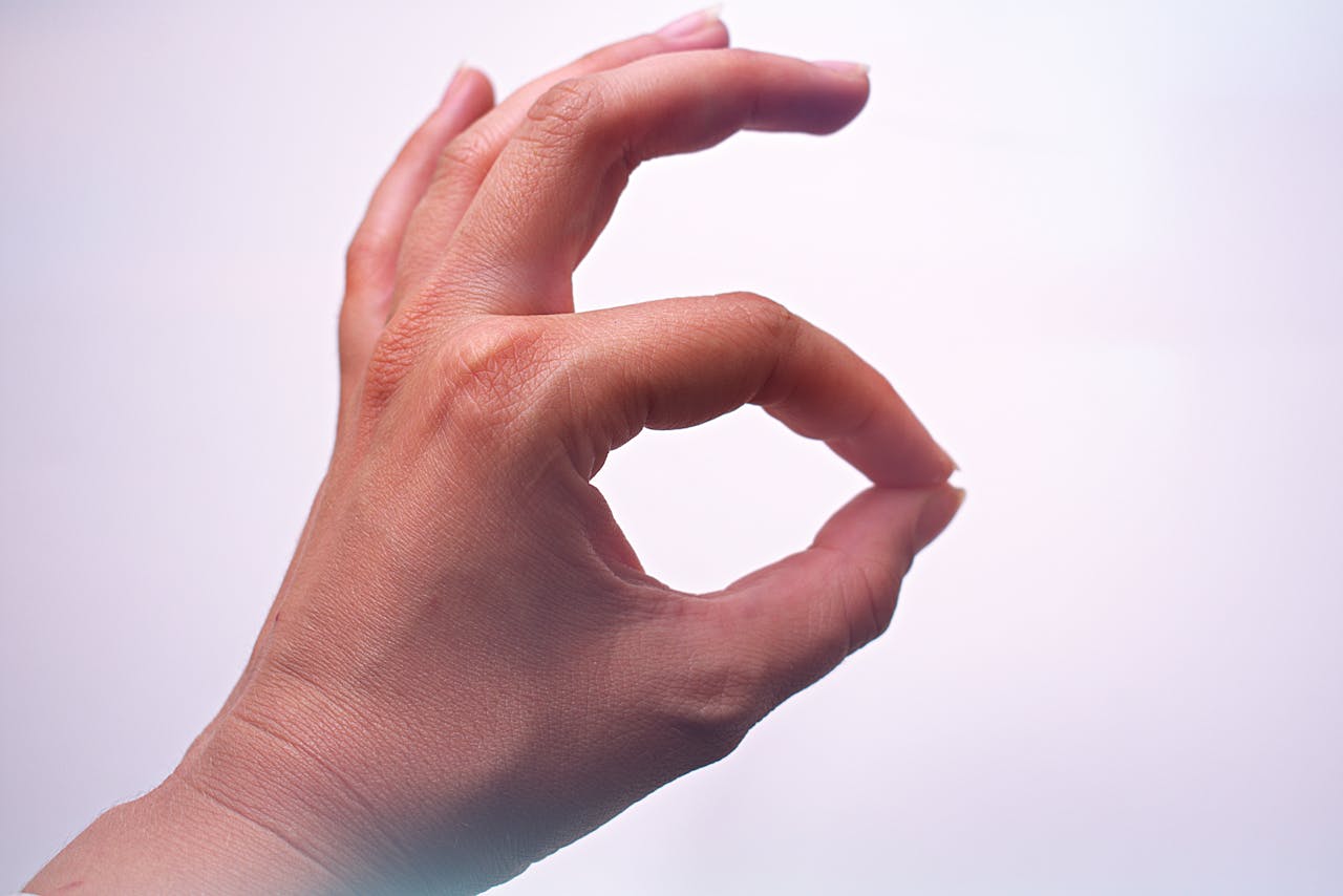 A close-up of a hand making an OK gesture, with a light background and soft lighting.